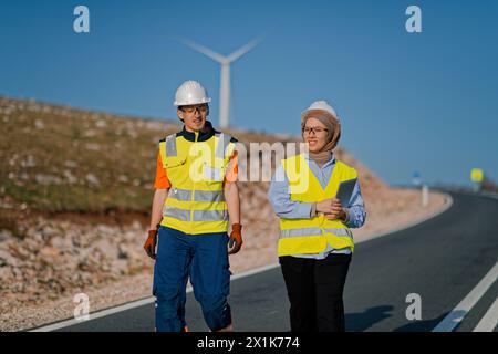 Une ingénieure avec une tablette et son collègue inspectent les éoliennes dans un champ, démontrant le travail d’équipe et le dévouement aux projets d’énergie renouvelable Banque D'Images