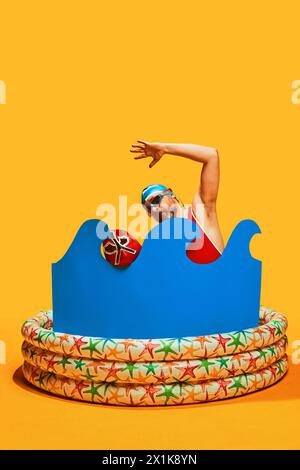 Nageur nage avec masque de lutte rouge dans la piscine pour enfants avec vague d'eau abstraite sur fond de studio jaune. Banque D'Images