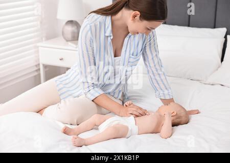 Jeune femme heureuse appliquant la crème pour le corps sur la peau du bébé sur le lit Banque D'Images