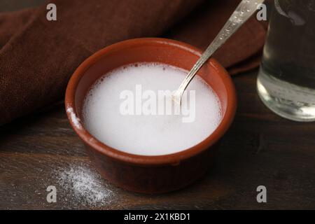 Réaction chimique du vinaigre et du bicarbonate de soude dans un bol sur une table en bois, gros plan Banque D'Images