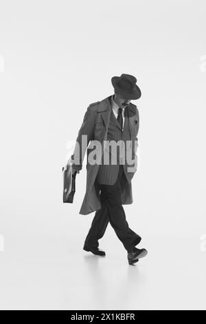 Homme en costume, chapeau Fedora et trench-coat marche avec porte-documents, capturant l'esthétique rétro. Banque D'Images