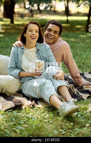 Couple diversifié dans une tenue vibrante assis ensemble sur une couverture, profitant d'un moment paisible dans le parc. Banque D'Images