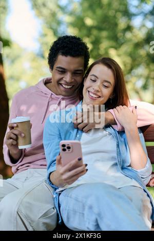 Couple diversifié dans une tenue vibrante assis sur le banc du parc, engrossed dans l'écran de téléphone portable. Banque D'Images