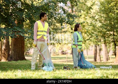 Un couple socialement actif et diversifié en gilets de sécurité et gants nettoyant le parc ensemble. Banque D'Images