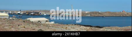 Un panorama du port de Luderitz avec des bateaux de pêche et des navires d'extraction de diamants avec l'ancien phare de Shark Island sur les rochers. Banque D'Images