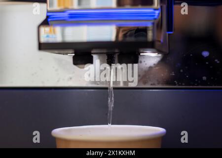 Une tasse bleue de café liquide est versée d'une machine dans un verre, créant une solution fluide pour une boisson rafraîchissante Banque D'Images
