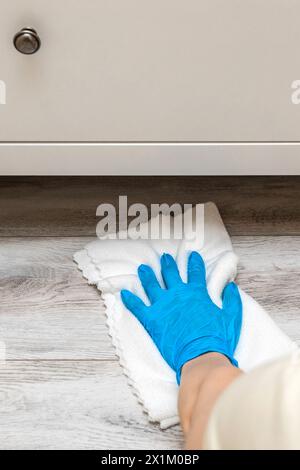 la femme au foyer portant des gants lave le sol sous le placard. nettoyage humide du sol dans la chambre. nettoyage de la poussière sous les armoires. Banque D'Images