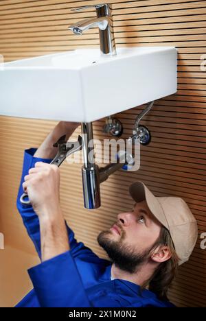 Bricoleur, plombier et outils dans l'évier de salle de bain avec clé, tuyaux et réparation au travail et au travail à la maison. Personne masculine, artisan et ouvrier pour le client dans Banque D'Images