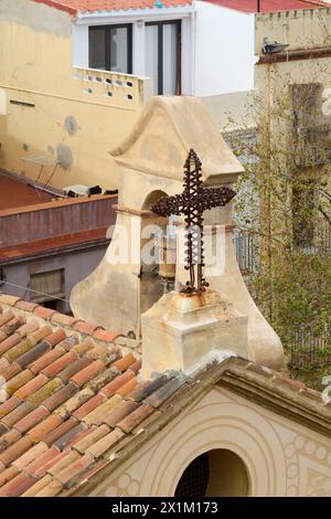 Une croix en métal ornée se distingue sur une toile de fond de bâtiments urbains il s perché au sommet d'un toit ancien avec des tuiles rouges et une str architecturale détaillée Banque D'Images