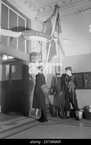 LA FILLE INCONNUE DERRIÈRE LA BATAILLE MARITIME : LE TRAVAIL DU SERVICE NAVAL ROYAL FÉMININ, 1942 - Wren Unknown arrive au HMS EAGLET et doit montrer sa passe à la sentinelle en service. Le panneau au-dessus de la porte indique «Bureau de l'officier du drapeau en charge», Royal Navy, EAGLET (HMS), établissement à terre Banque D'Images