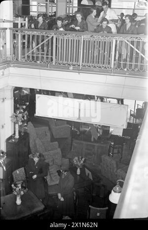 DES FAUTEUILS AUX BOMBARDIERS : TRAVAIL DE GUERRE À LA SALLE D'EXPOSITION DE MEUBLES PERRINGS, KINGSTON, SURREY, 1943 - des travailleuses de guerre à temps partiel produisent des câbles et d'autres équipements électriques pour les bombardiers de la Royal Air Force à l'étage supérieur de cette salle d'exposition de meubles. Un superviseur vérifie que tout va bien, que les affaires de vente de meubles se poursuivent en dessous d'eux, Banque D'Images