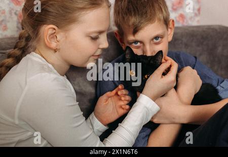 Un garçon et une fille sont assis sur un canapé, avec un chat niché entre eux. Ils semblent détendus et contents, appréciant les uns les autres compagnie dans une vie confortable Banque D'Images