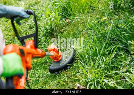 Jardinier utilisant un coupe-herbes électrique pour couper l'herbe dans le jardin. Entretien de pelouse dans la cour Banque D'Images