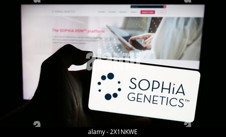 Personne tenant un smartphone avec le logo de la société suisse de logiciels de santé Sophia Genetics sa en face du site. Concentrez-vous sur l'affichage du téléphone. Banque D'Images