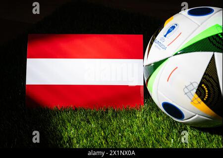 LEIPZIG, ALLEMAGNE, 17 AVRIL 2024 : drapeau national autrichien et ballon officiel de football de l'Euro 2024 en Allemagne placé sur l'herbe verte. BL Banque D'Images