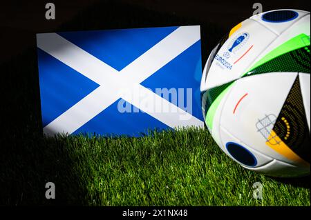 HAMBOURG, ALLEMAGNE, 17 AVRIL 2024 : drapeau national écossais et ballon officiel de football de l'Euro 2024 en Allemagne placés sur l'herbe verte. B Banque D'Images