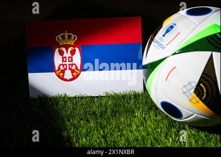 LEIPZIG, ALLEMAGNE, 17 AVRIL 2024 : drapeau national de Serbie et ballon officiel de football de l'Euro 2024 en Allemagne placé sur l'herbe verte. Bla Banque D'Images