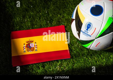 LEIPZIG, ALLEMAGNE, 17 AVRIL 2024 : drapeau national espagnol et ballon officiel de football de l'Euro 2024 en Allemagne placé sur l'herbe verte. Blac Banque D'Images