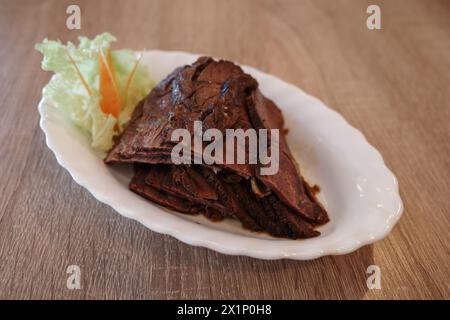 Une délicieuse portion de rôti de bœuf finement tranché, soigneusement disposé sur une assiette ovale blanche, accompagnée d'une simple garniture de laitue et de bâtonnets de carottes. Banque D'Images