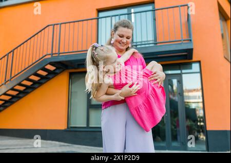 Heureuse mère balançant et filant fille mignonne en cercles par les bras à l'extérieur. Gamin ludique énergique et joyeux s'amusant tout en se liant à maman Banque D'Images