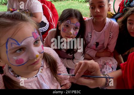 Bucarest, Roumanie. 17 avril 2024 : une fille ukrainienne (l) a son visage peint par un artiste lors de l'ouverture du Centre de jour pour les enfants réfugiés d'Ukraine dont les mères travaillent ou veulent trouver un emploi. Le centre est ouvert par la Fondation Save the Children Roumanie pour 40 enfants, âgés de 6 à 11 ans, et pour soutenir les mères réfugiées d'Ukraine afin qu'elles puissent laisser leurs enfants en toute sécurité pendant qu'elles sont au travail, compte tenu du fait que trois parents ukrainiens sur cinq ne pouvaient pas trouver un emploi en Roumanie, la plupart d’entre eux citant la barrière de la langue ou la nécessité de prendre soin d’une famille moi Banque D'Images