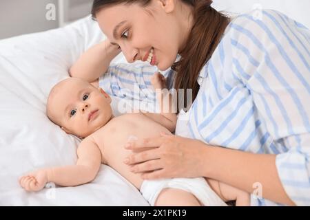 Jeune femme heureuse appliquant la crème pour le corps sur la peau du bébé sur le lit Banque D'Images