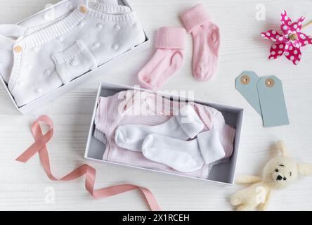 Boîte avec des trucs de bébé et des accessoires pour nouveau-né sur fond en bois blanc. Boîte cadeau avec vêtements, chaussettes et lapin jouet tricoté. Concept de douche de bébé. Banque D'Images