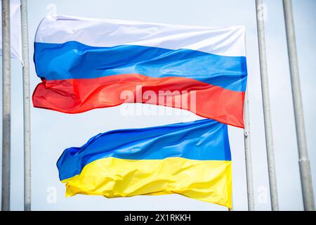 Les drapeaux russes et ukrainiens agitent de vent au-dessus du ciel bleu. Vue en angle bas. Concept de différend et de conflit. Composition horizontale avec espace de copie. Banque D'Images