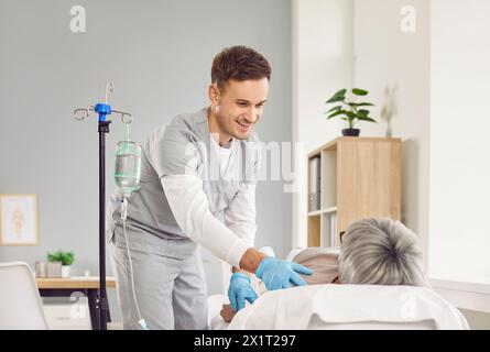 Jeune infirmière prenant soin d'un patient âgé allongé sur le lit et recevant une perfusion intraveineuse Banque D'Images