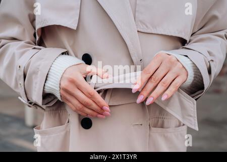 Détails de fantaisie de style urbain d'un trench beige pour femme avec ceinture. Tissu tendance contemporain Banque D'Images