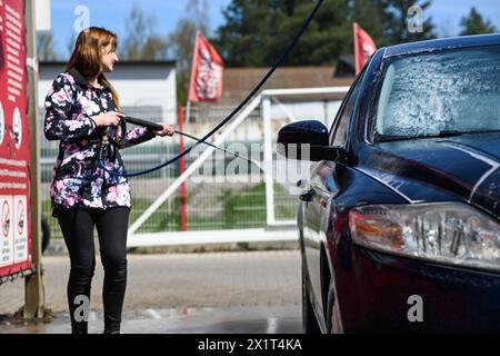 une femme lave une voiture dans un lave-auto. Elle tient un pistolet à eau à pression dans sa main. Banque D'Images