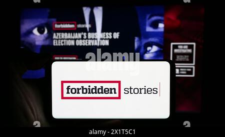 Personne tenant un téléphone portable avec le logo de l'organisation de journalisme d'investigation histoires interdites devant la page Web. Concentrez-vous sur l'affichage du téléphone. Banque D'Images