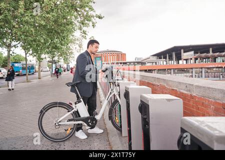 Jeune homme latin louant un vélo à une machine de service de location de vélos. il utilise son téléphone intelligent pour déverrouiller le vélo. Concept de vie urbaine. Banque D'Images
