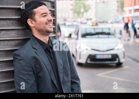 joyeux homme latin en blazer riant alors qu'il est soutenu et attend Banque D'Images
