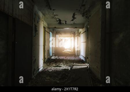 Couloir délabré dans un bâtiment abandonné avec la lumière du soleil coulant à travers l'extrémité. Banque D'Images