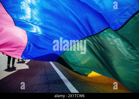 Un grand drapeau de fierté éclatant jaillit dans la brise lors d'un défilé, avec les jambes des gens visibles en dessous Banque D'Images