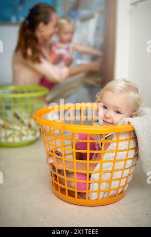 Bébé heureux, portrait et panier à linge avec maman pour l'enfance amusante, jeu ou journée de corvée à la maison. Jeune, petite fille et sourire dans le seau avec la mère ou Banque D'Images