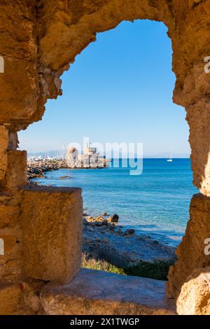 Vue sur la baie de Rhodes à travers une fenêtre dans un mur rocheux. En arrière-plan, la mer et le moulin à vent dans le port Mandraka Banque D'Images