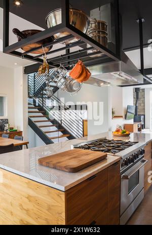 Île en bois de noyer américain avec comptoir de quartzite et cuisinière à gaz intégrée dans la cuisine à l'intérieur de la maison de style cube moderne, Québec, Canada Banque D'Images