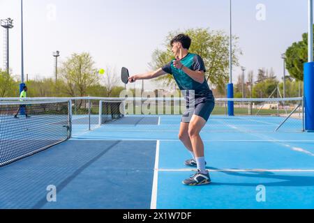 Vue latérale d'un jeune homme en forme jouant au pickleball dans un court extérieur Banque D'Images