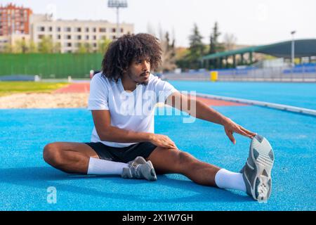 Jeune homme sportif beau avec coiffure africaine s'étirant dans une piste de course Banque D'Images