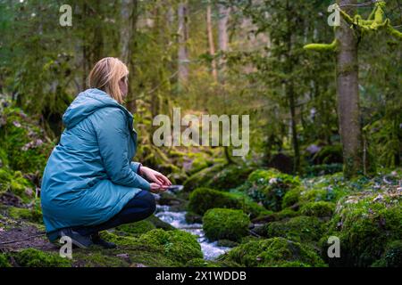 Une femme est assise sur la rive d'un ruisseau forestier, entourée de mousse et de végétation verte, et semble penser, Calw, Forêt Noire, Allemagne Banque D'Images