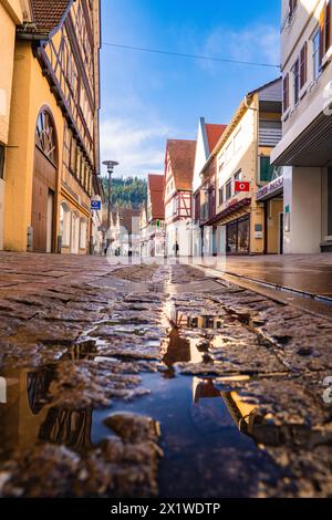 Vue sur la rue d'un village européen avec des maisons traditionnelles à colombages et une flaque reflétant le ciel bleu, printemps, Calw, Forêt Noire, Allemagne Banque D'Images