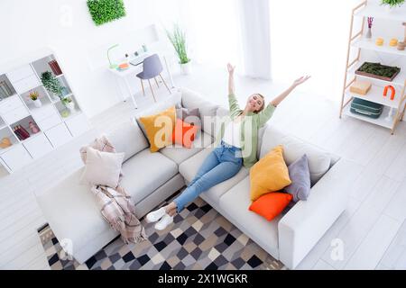 Photo à angle élevé de jeune femme au foyer souriante belle dame levé les bras vers le haut acheté un nouvel appartement avec des choses intérieures de conception loft à l'intérieur Banque D'Images