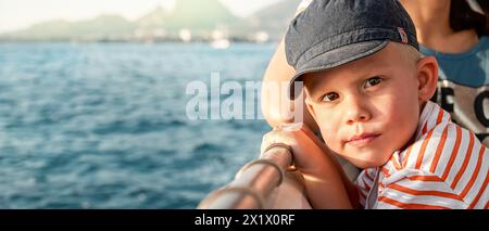 Mignon tout-petit avec mère aime le voyage en bateau naviguant dans la mer au-delà de la côte de Marmaris. Portrait d'un garçon en casquette de protection solaire en vacances en Turquie grand plan Banque D'Images