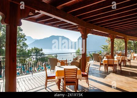 Vue matinale sur la terrasse en bois d'un hôtel de bord de mer avec tables à manger, surplombant la mer et les collines Banque D'Images