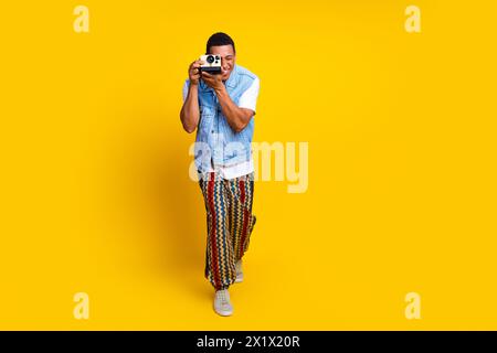 Photo de joyeux gars habillé gilet de jeans tenant la caméra rétro sur l'oeil capturant des photos isolées sur fond de couleur jaune vif Banque D'Images