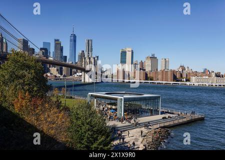 Parc d'attractions Janes Carousel tour à Brooklyn Bridge Park, Brooklyn avec Brooklyn Bridge, East River et Lower Manhattan gratte-ciel derrière, New York Banque D'Images