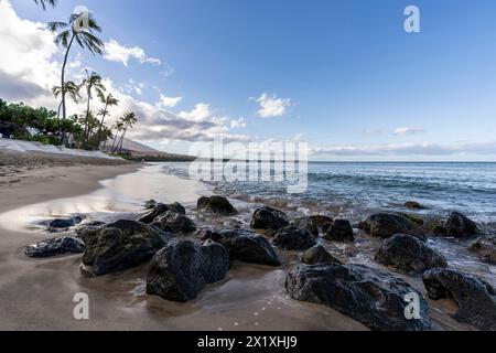 Les vagues s'écrasent sur de grandes roches volcaniques noyées dans le sable le long d'une plage à Lahaina, Hawaï, États-Unis Banque D'Images