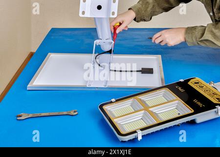 Assemblant le lampadaire solaire autonome, un électricien attache le module solaire et le luminaire LED au bras de lumière ou au support de montage. Banque D'Images